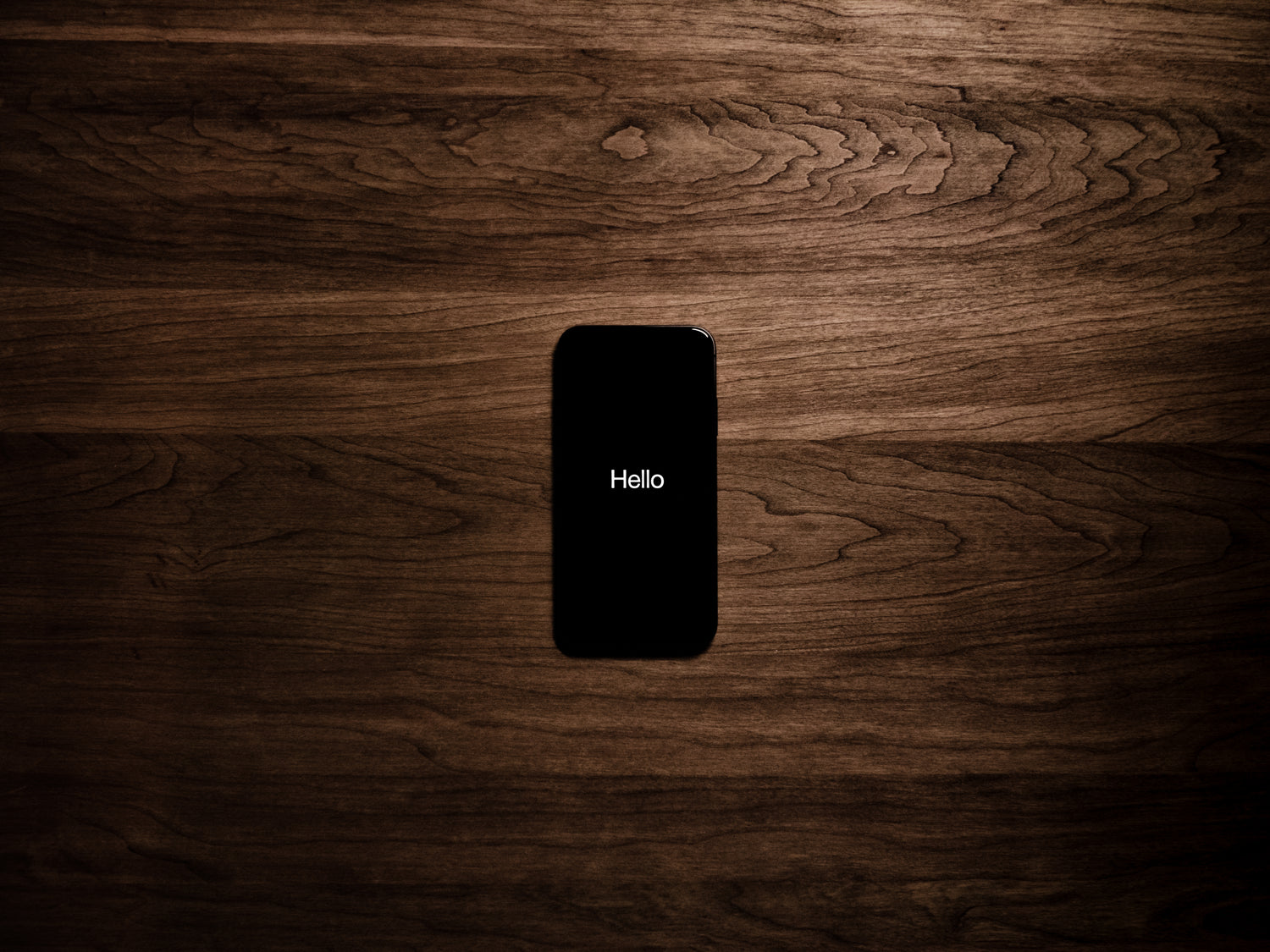 Smartphone auf Holzplatte mit Text "Hello"!